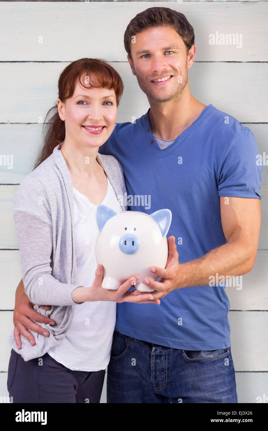 Composite image of couple holding a white piggy bank Stock Photo - Alamy