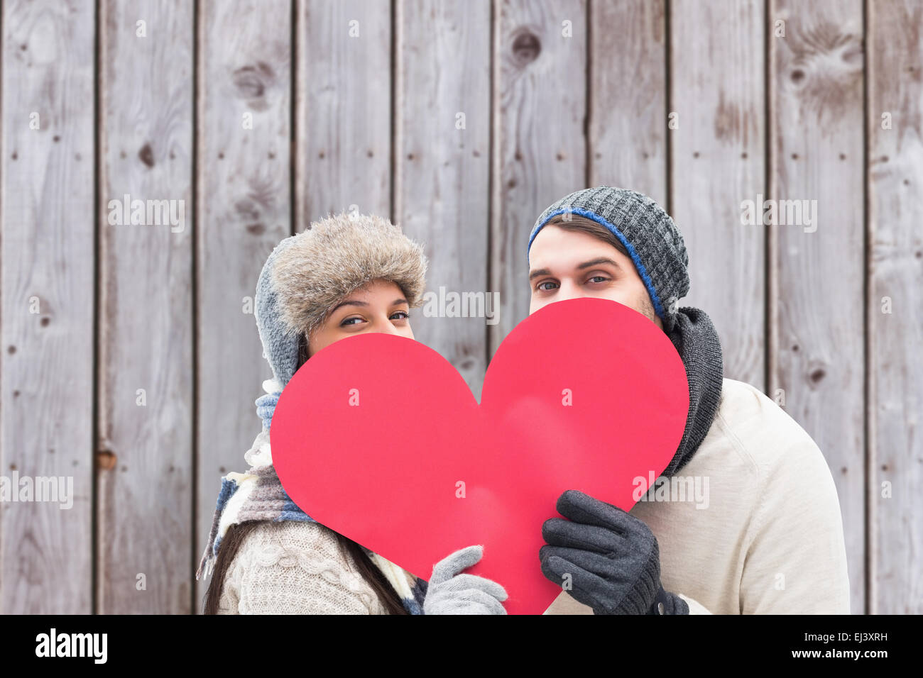Composite image of attractive young couple in warm clothes holding red heart Stock Photo