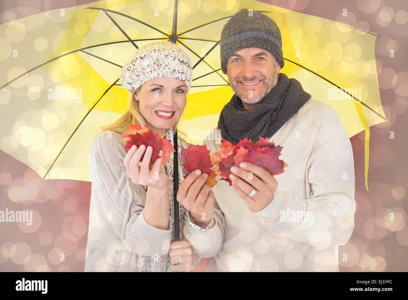 Composite image of couple in winter fashion showing autumn leaves under umbrella Stock Photo