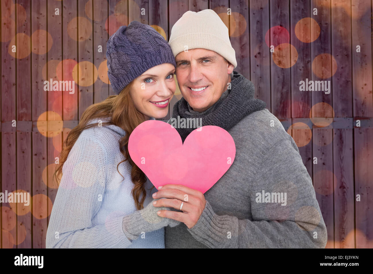 Composite image of happy couple in warm clothing holding heart Stock Photo