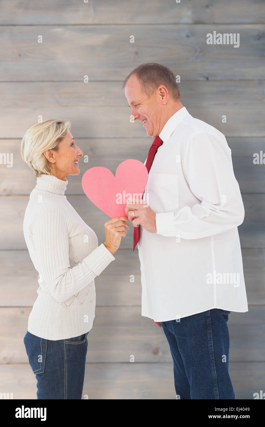 Composite image of older affectionate couple holding pink heart shape Stock Photo