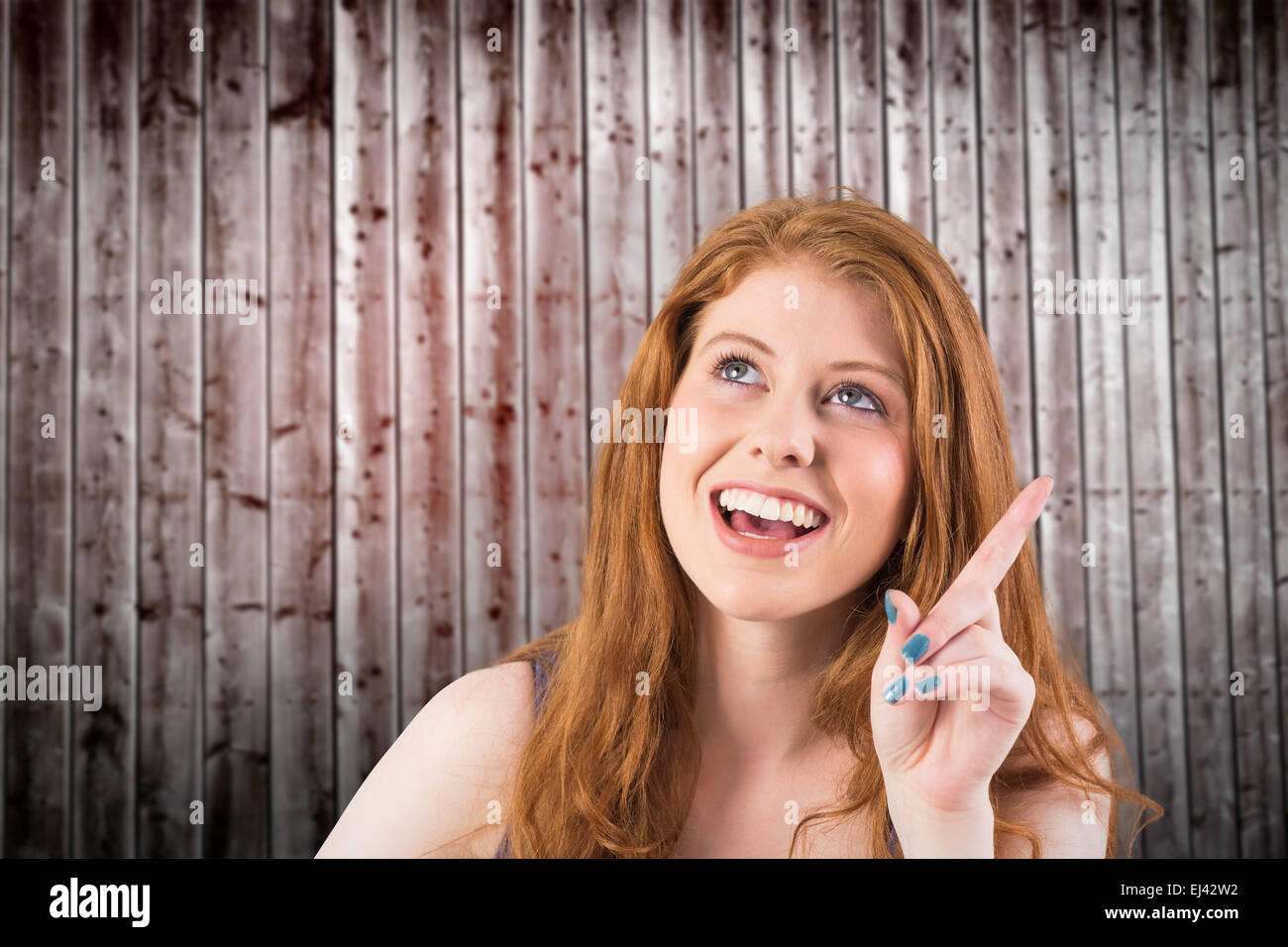 Composite image of pretty redhead pointing and looking up Stock Photo