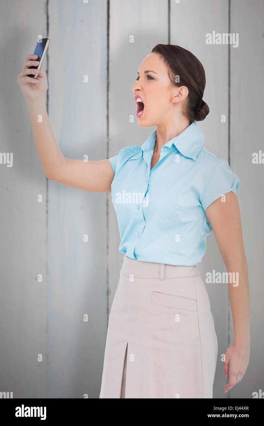 Composite image of angry classy businesswoman yelling at her smartphone Stock Photo
