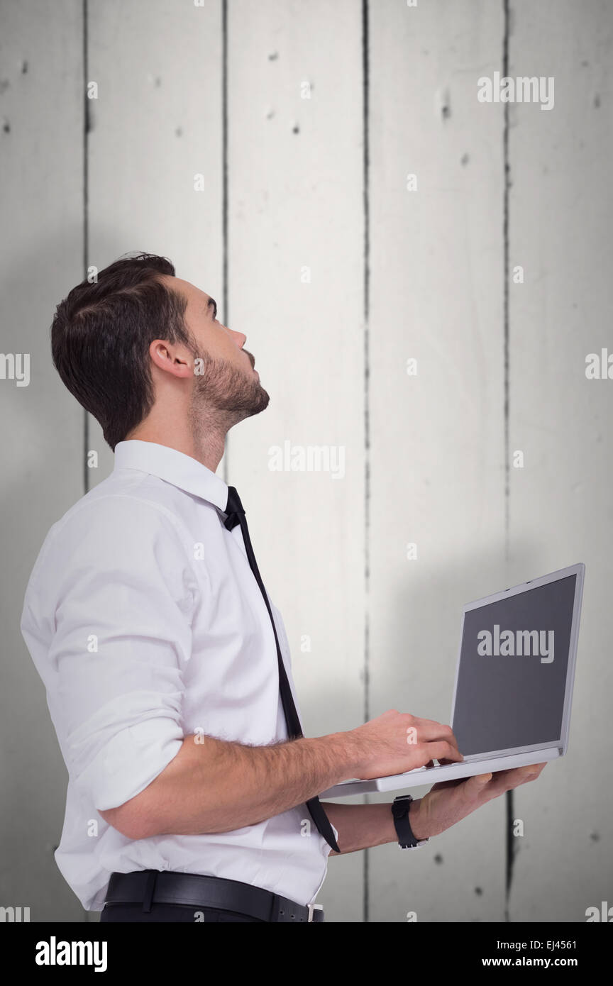 Composite image of sophisticated businessman standing using a laptop Stock Photo