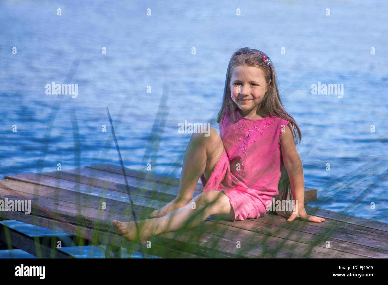 little girl sitting near lake in summer outdoors Stock Photo