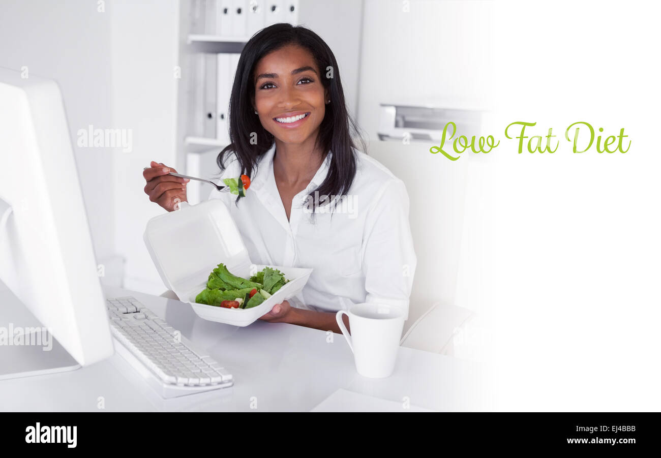Low fat diet against happy pretty businesswoman eating a salad at her desk Stock Photo