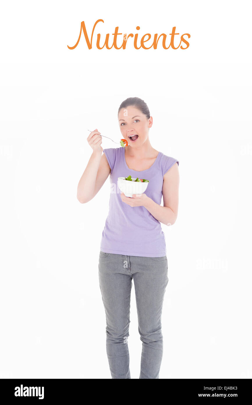 Nutrients against gorgeous woman eating a bowl of salad while standing Stock Photo