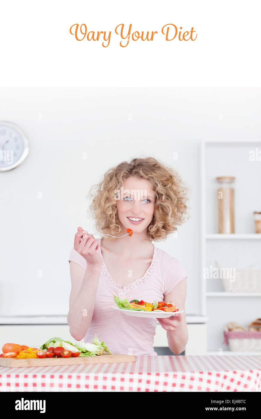 Vary your diet against pretty blonde woman eating some vegetables in the kitchen Stock Photo