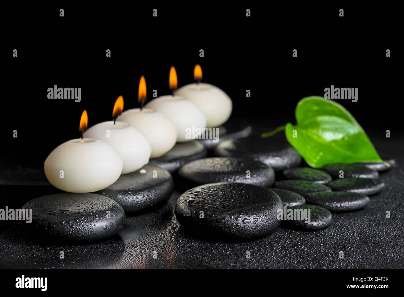 spa concept of row white candles and green leaf Calla lily on black zen