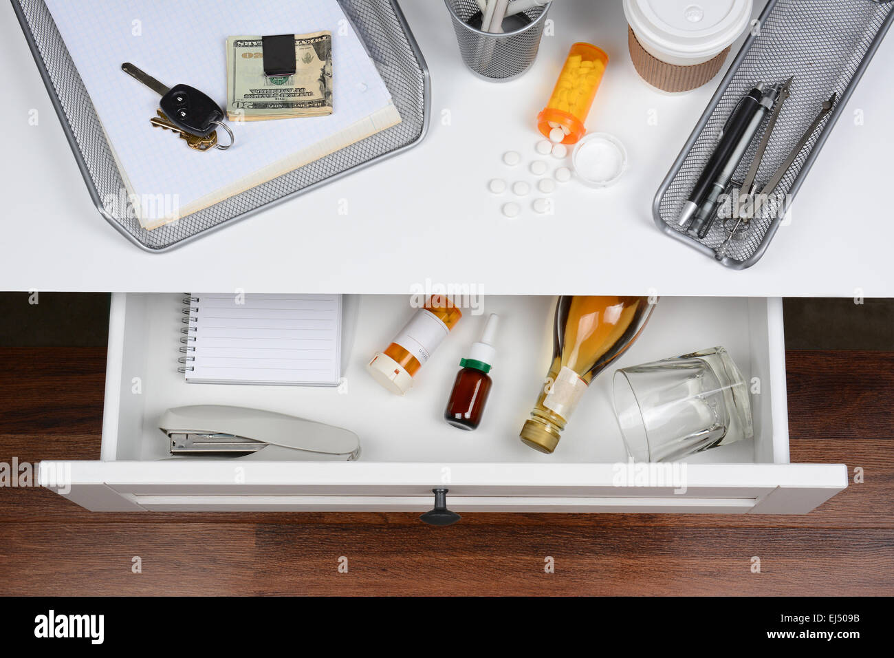 High angle shot of an open desk drawer showing the items inside. The top of the desk has a coffee cup, spilled prescription bott Stock Photo