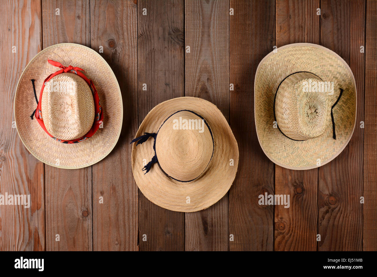 Three straw hats hanging on a rustic wood farmhouse wall. Closeup in horizontal format. Stock Photo