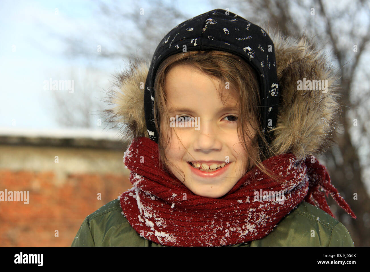 Preschool girl with auburn hair and brown eyes is playing with snow outside in a winter day. He is dressed with warm winter clot Stock Photo