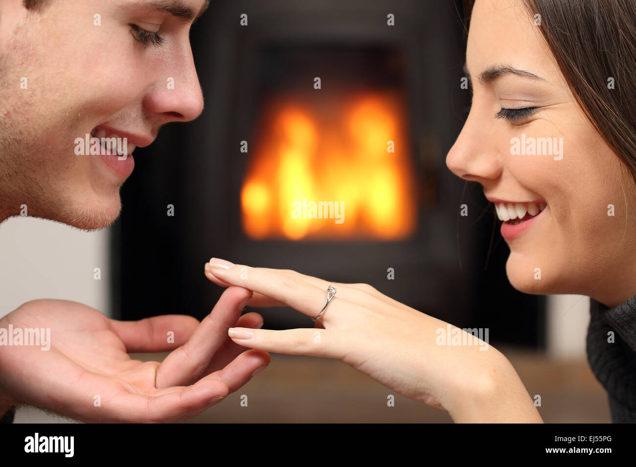 Couple looking a engagement ring after proposal at home with a fire place in the background Stock Photo