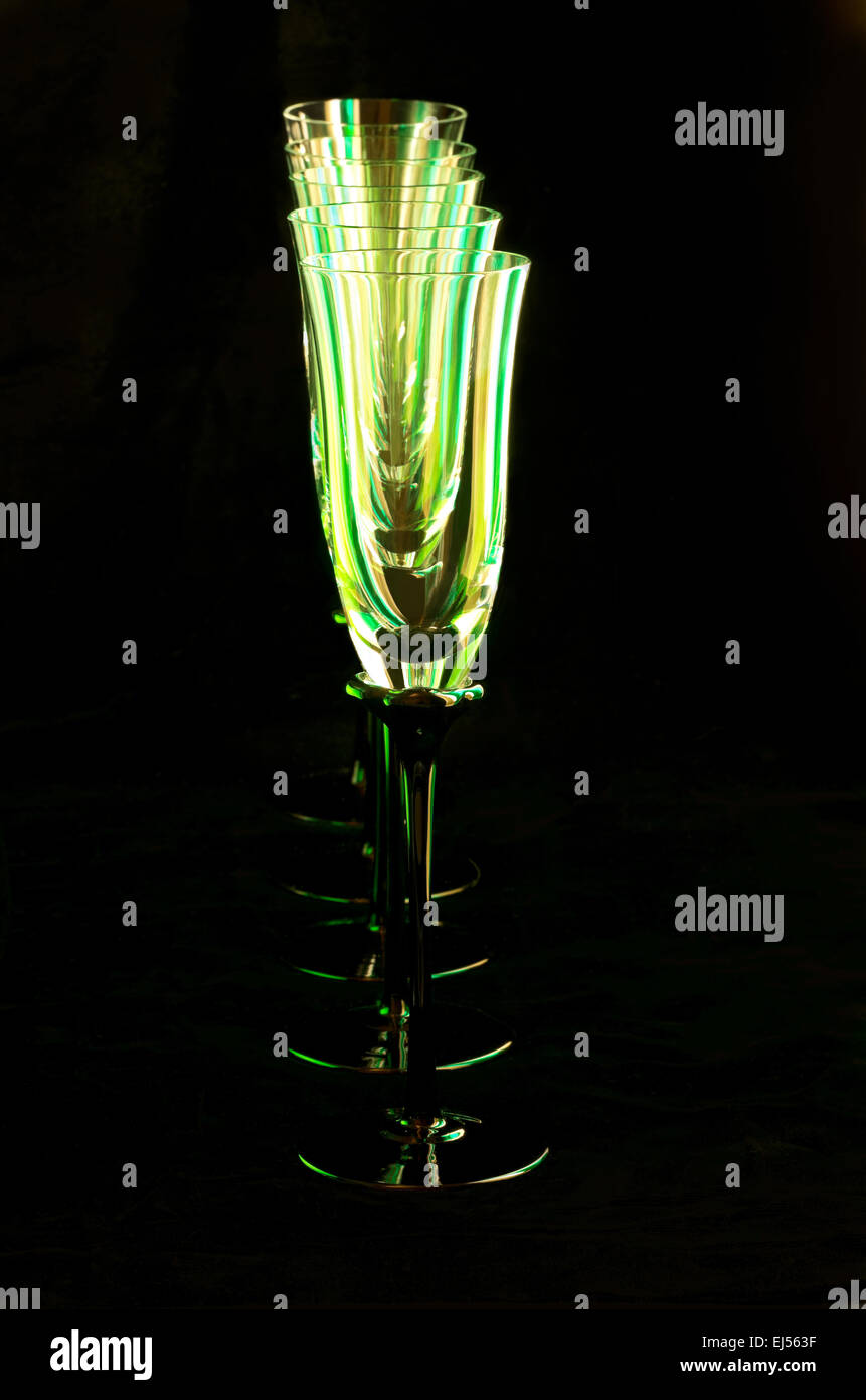 Abstract of flute glasses or champagne stemware with green reflections lined up in a column isolated against black Stock Photo