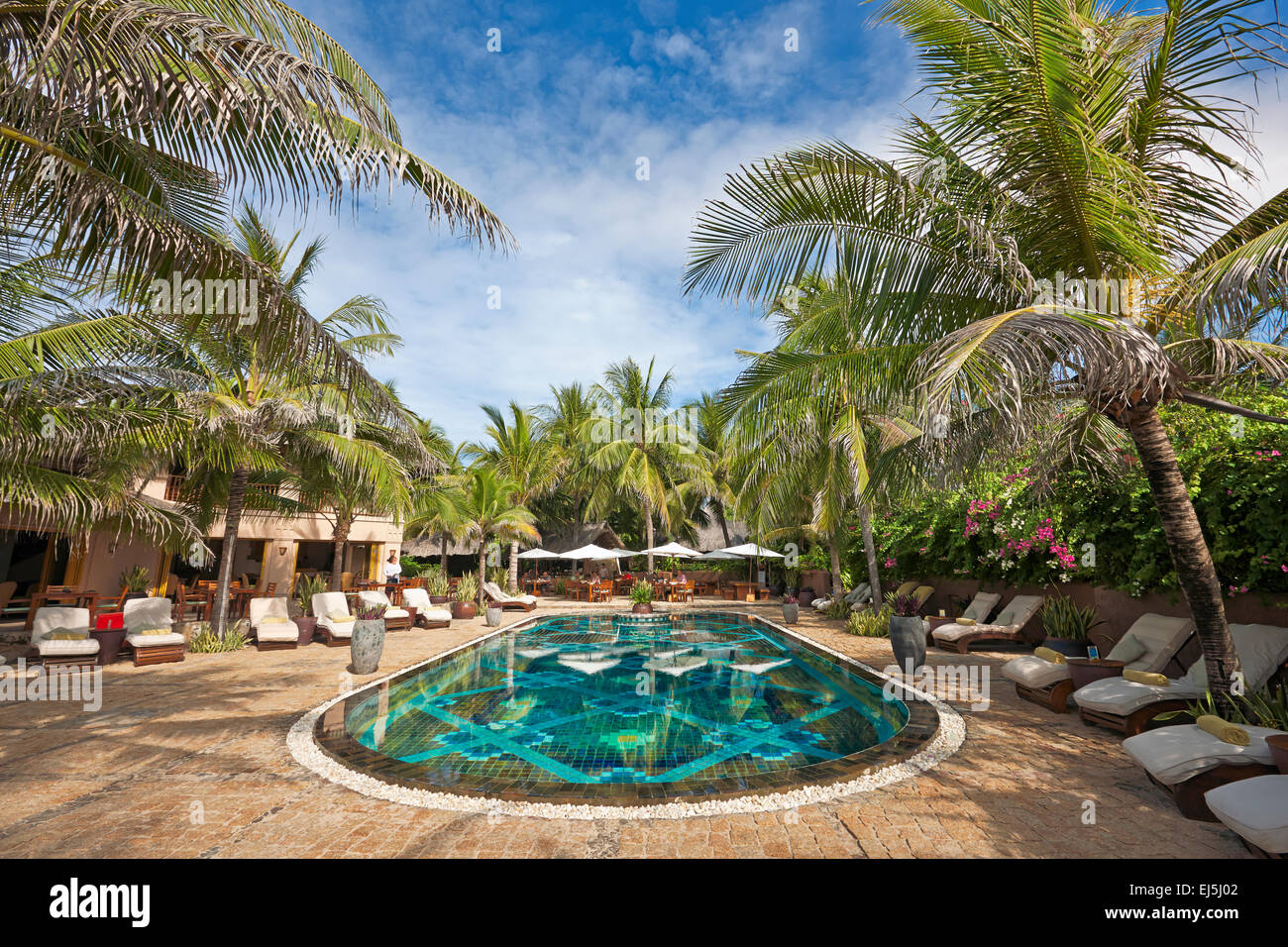 Swimming pool area with lounge chairs surrounded by palm trees in Mia Resort Mui Ne. Mui Ne, Binh Thuan Province, Vietnam. Stock Photo