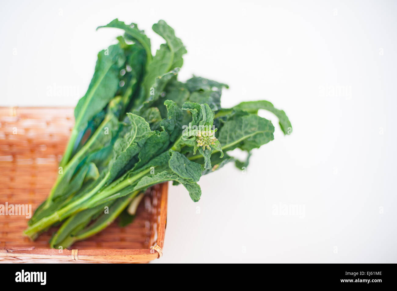 Bunch of green kale in brown basket on white background with focus on flower Stock Photo