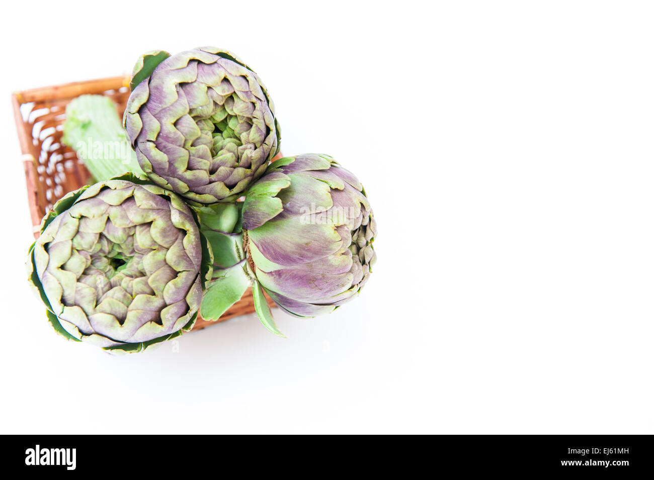 Bunch of three artichokes in brown basket on white background and copyspace on the right Stock Photo