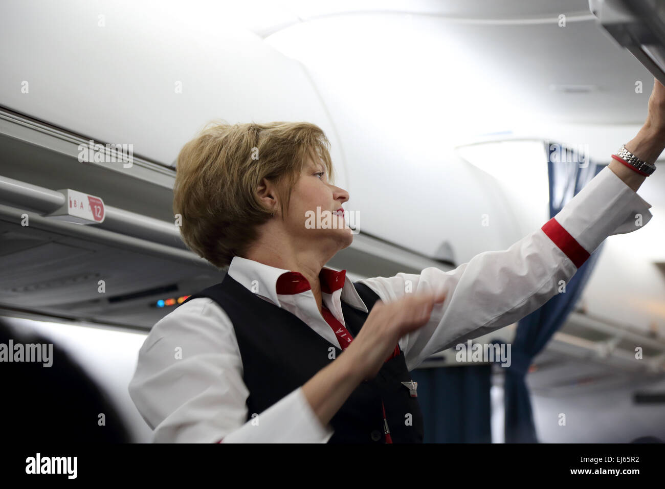 Female flight attendant closes overhead carry-on bins on airplane flight Stock Photo