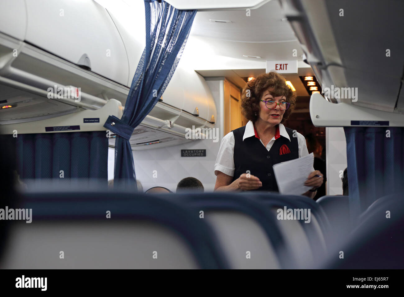 Female flight attendant talks to airline passengers from the aisle in the airplane Stock Photo