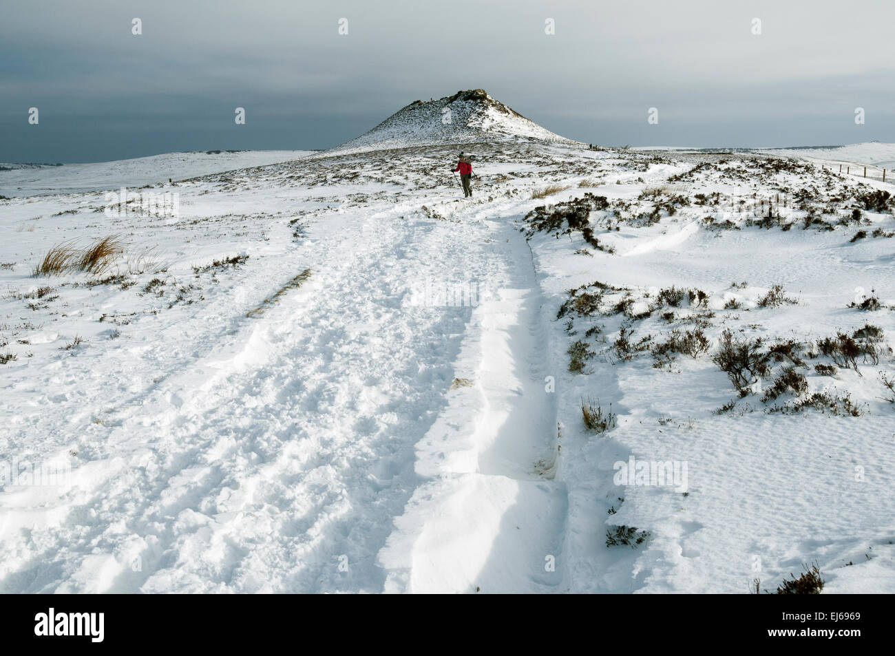 A walker on the west ridge of Win Hill in winter, Peak District, Derbyshire, England, UK. Win Hill summit behind. Stock Photo