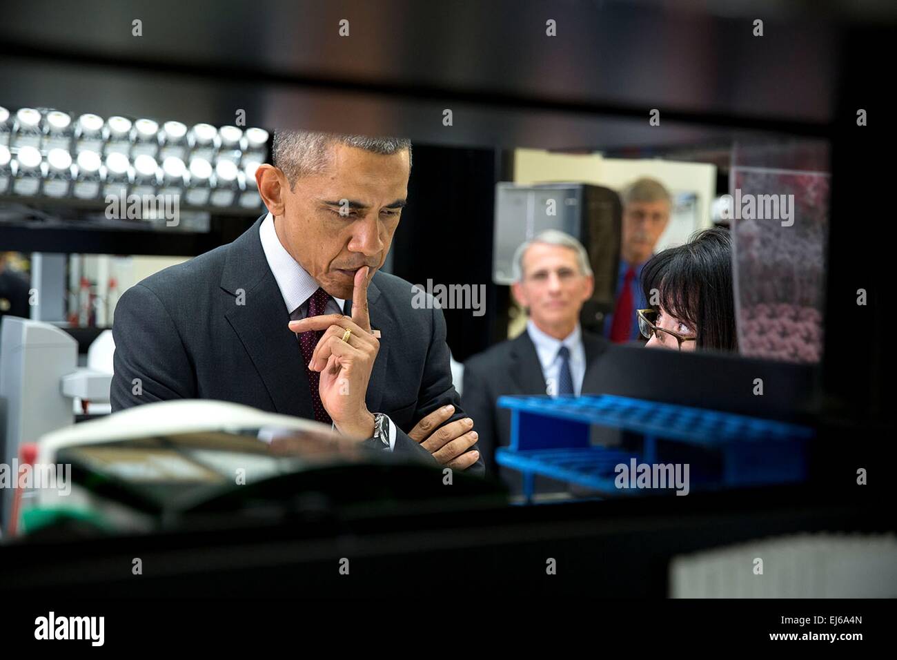 US President Barack Obama listens to Dr. Nancy Sullivan, Senior Investigator, Chief Biodefense Research Section, explain the investigational Ebola vaccine candidate currently being tested on humans during a lab tour at the Vaccine Research Center at the National Institutes of Health December 2, 2014 in Bethesda, Maryland. Dr. Anthony Fauci, Director, National Institute of Allergy and Infectious Diseases and Dr. Francis Collins, Director, NIH watch in the background. Stock Photo