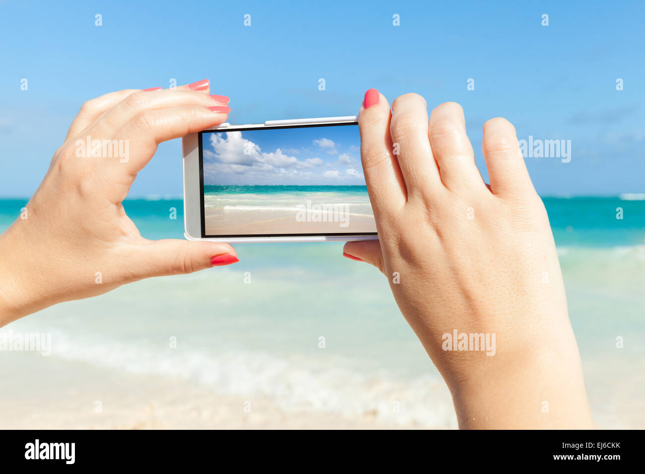 Woman using cell phone for taking sea landscape photo on a beach in