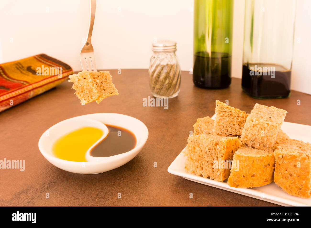 Photo of dipping bread cubes into oil and vinegar on white plates and