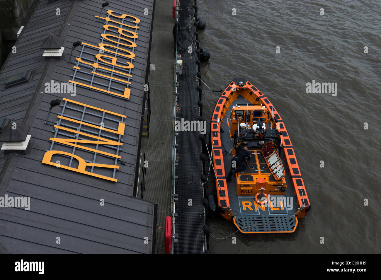 A new RNLI Lifeboat moored up, in the river Thames why a crew member works on getting it ship ready. Stock Photo