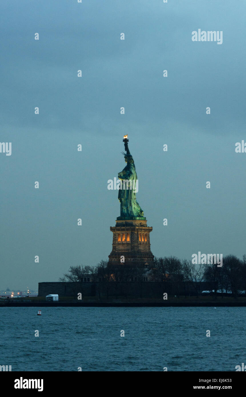 The lights of the Statue of Liberty glow in the blue haze of rainy twilight, New York City. Stock Photo
