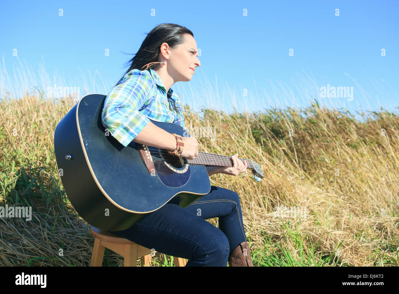 Country hippie girl with guitar at wheat field drinking black ca Stock Photo