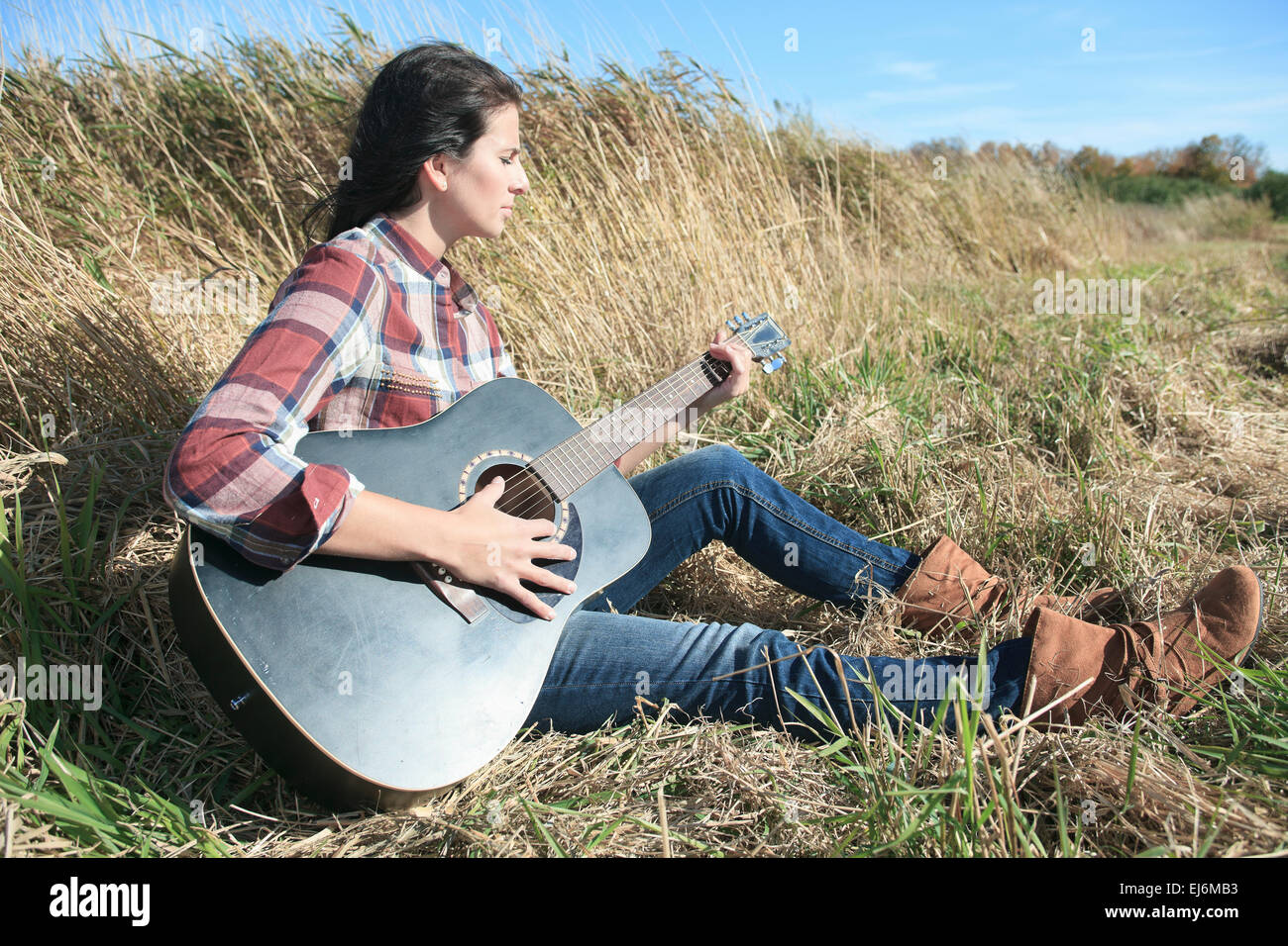 Country hippie girl with guitar at wheat field drinking black ca Stock Photo