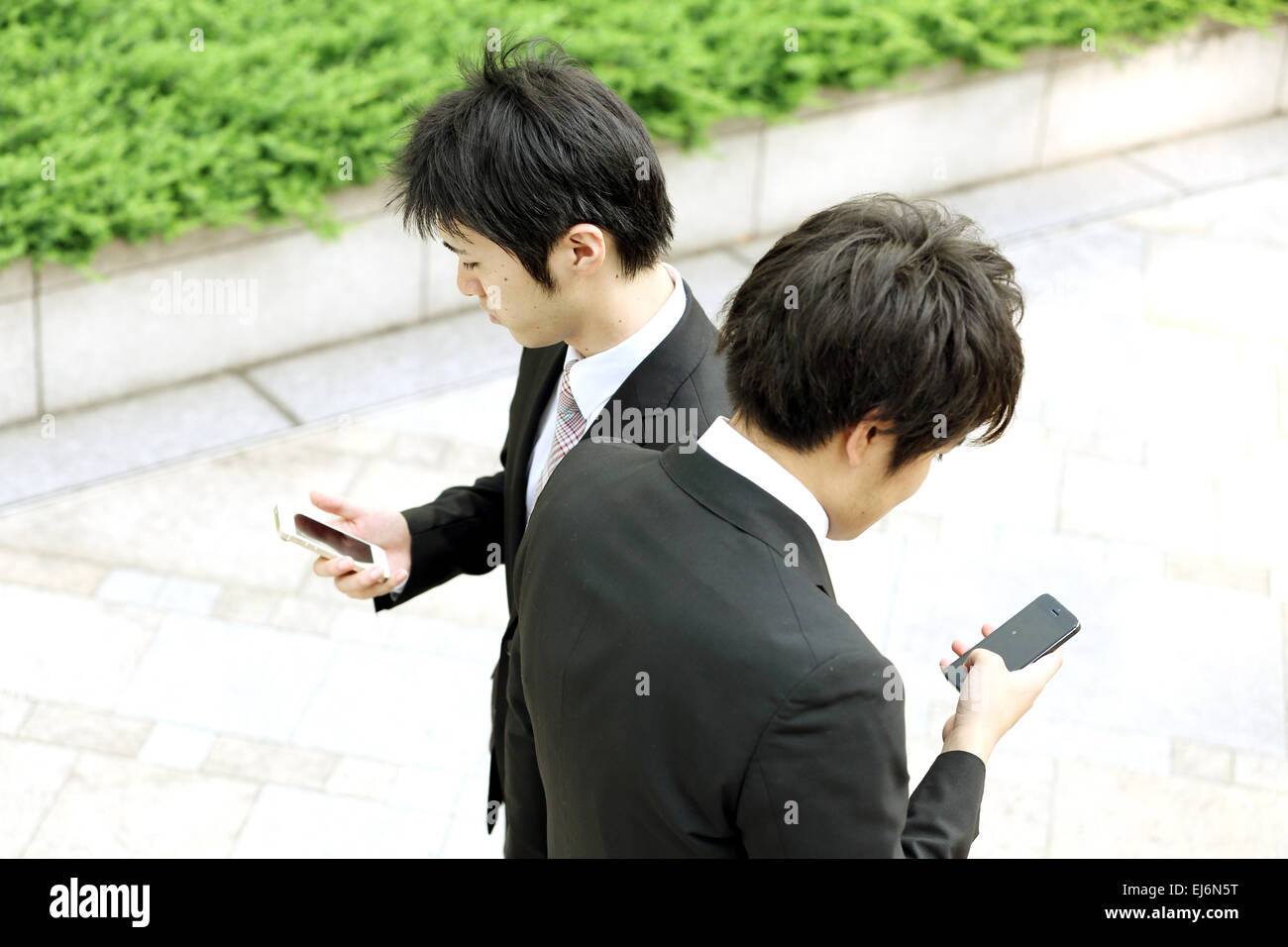 Two Japanese men hitting each other while walking with smartphones Stock Photo