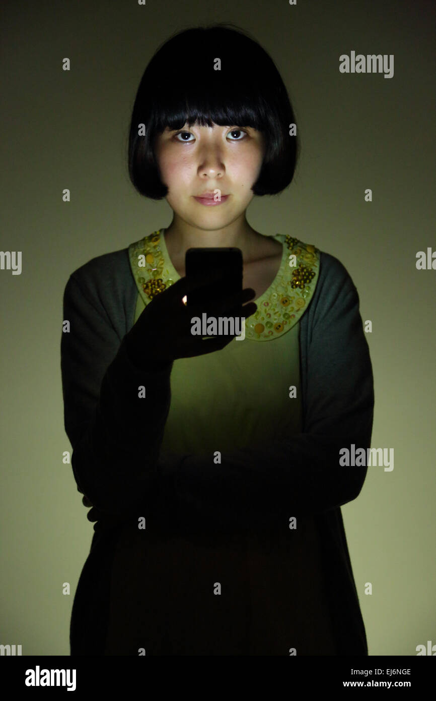 Young Japanese girl in a dark room with smartphone Stock Photo