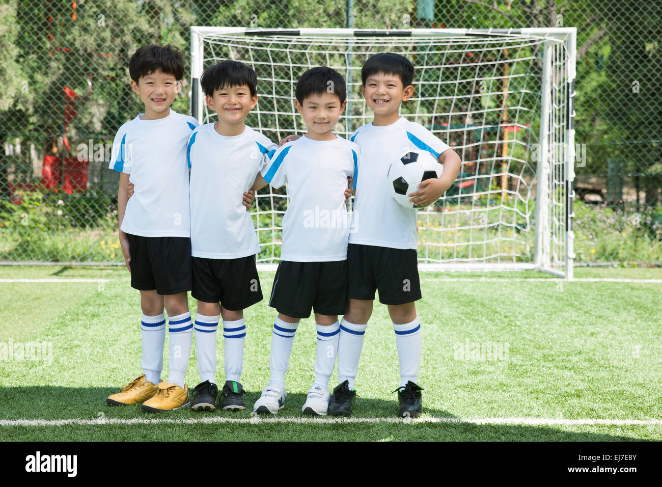 Four boys hug shoulders stood on the football field Stock Photo