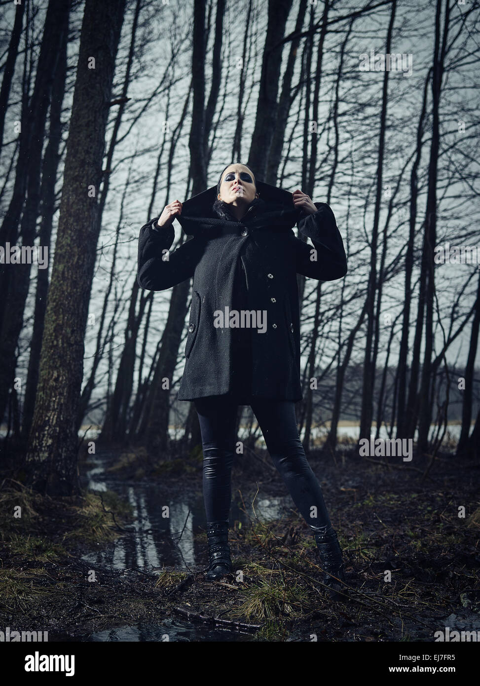 Fashion woman wearing a winter coat and she standing in a gloomy forest ...