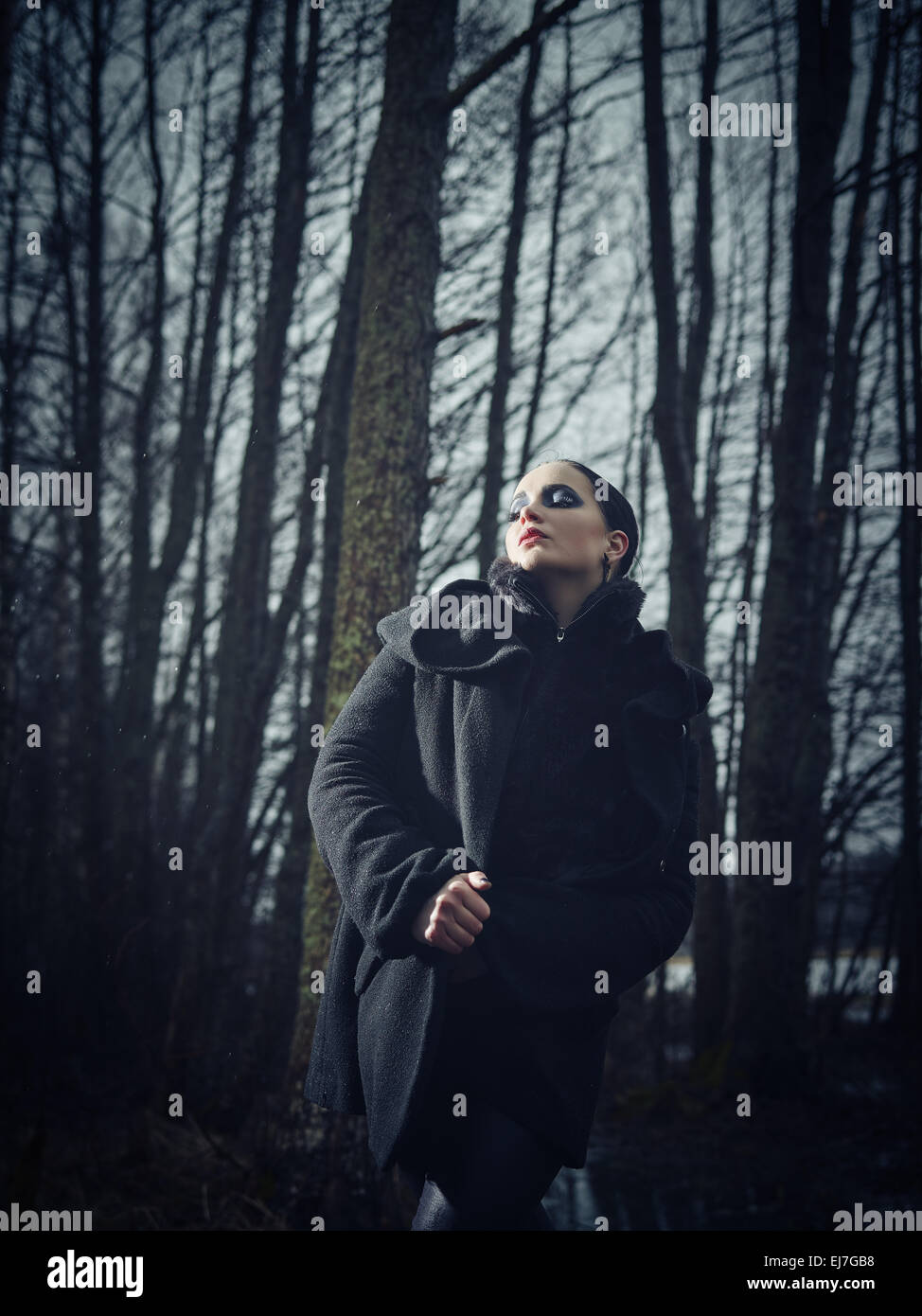 Fashion woman wearing a winter coat and she pose in a gloomy forest, cold rainy weather, cross processed full length image Stock Photo