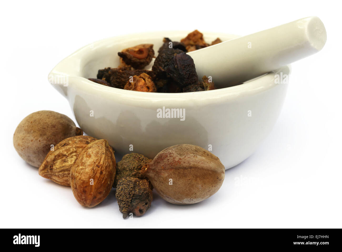 Triphala, a combination of ayurvedic fruits with mortar and pestle over white background Stock Photo
