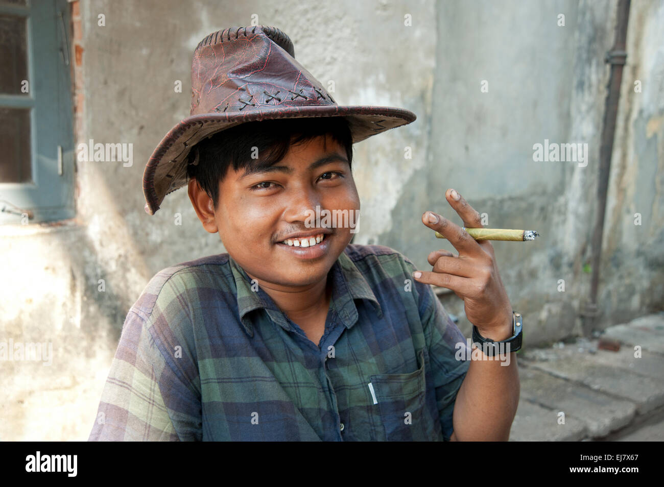 Happy smiling portrait of young Burmese man holding cheroot and wearing a hat on the streets of Yangon Myanmar Burma Stock Photo