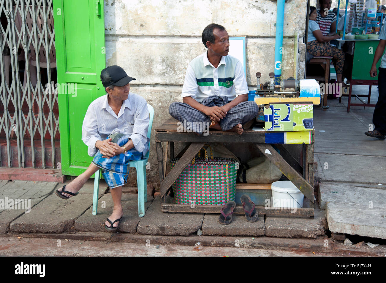 Two Burmese streets vendors sit by their stall in  a Rangoon side street Myanmar Stock Photo