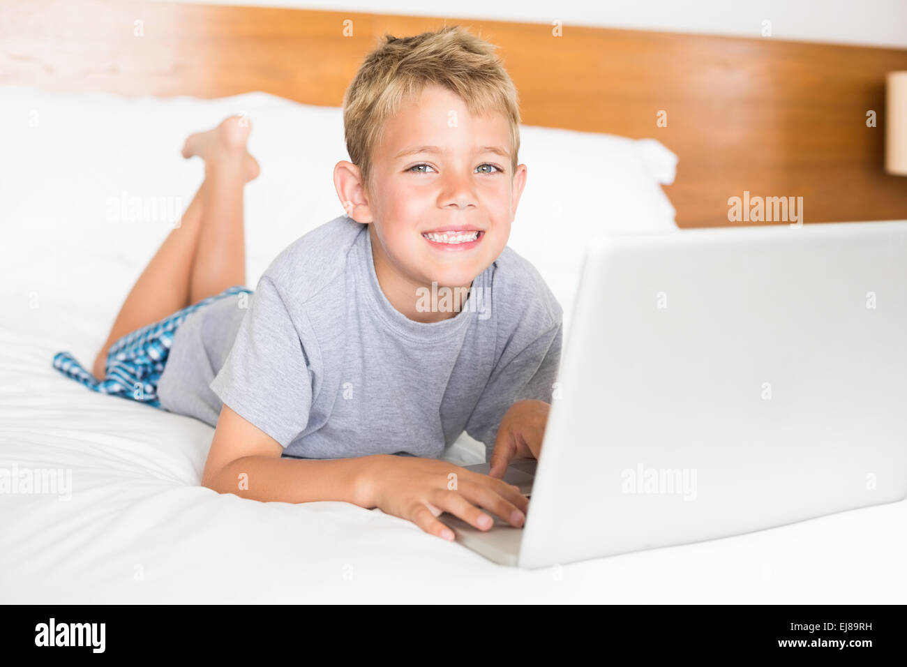 Happy blonde boy lying on bed using laptop Stock Photo - Alamy