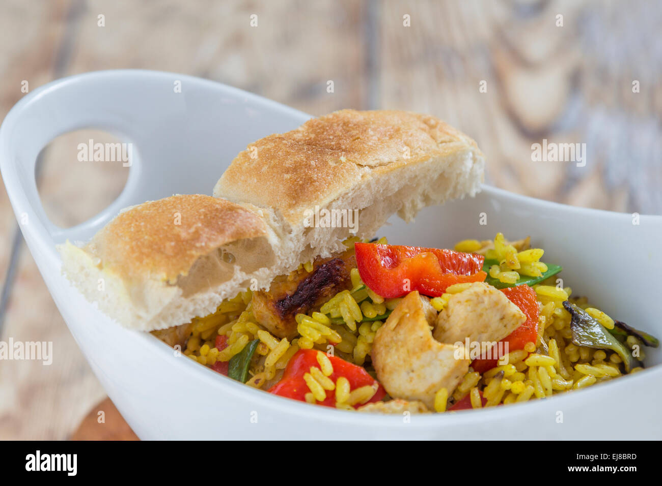 Bowl with curry flavored rice chicken and vegetables on rustic wooden table Stock Photo
