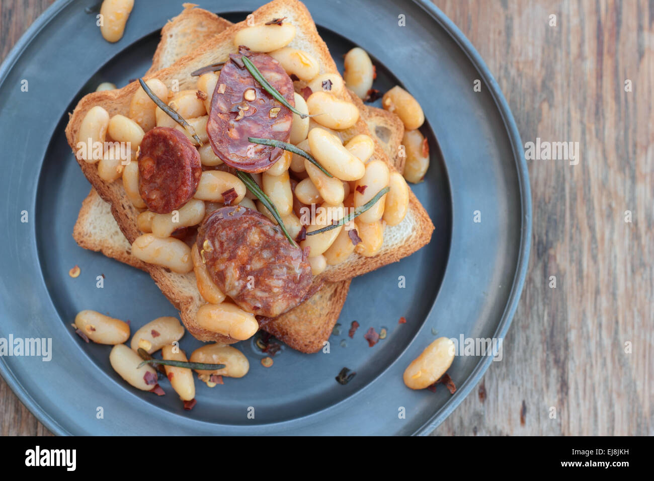 Toast with beans and chorizo cooked with rosemary leaves on a tin plate