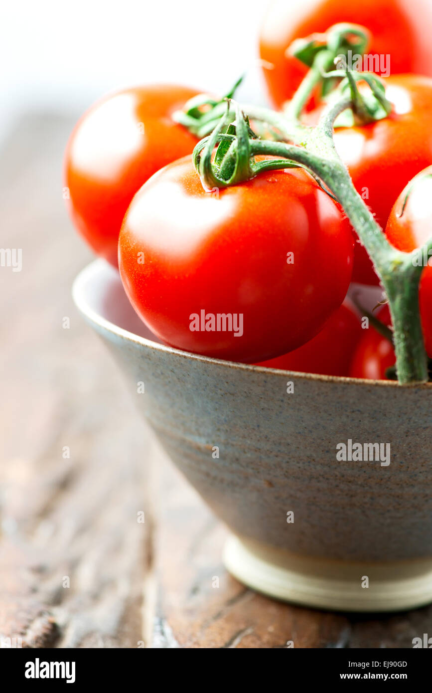 Tomatoes in a bowl on old wooden table vertical high key Stock Photo ...
