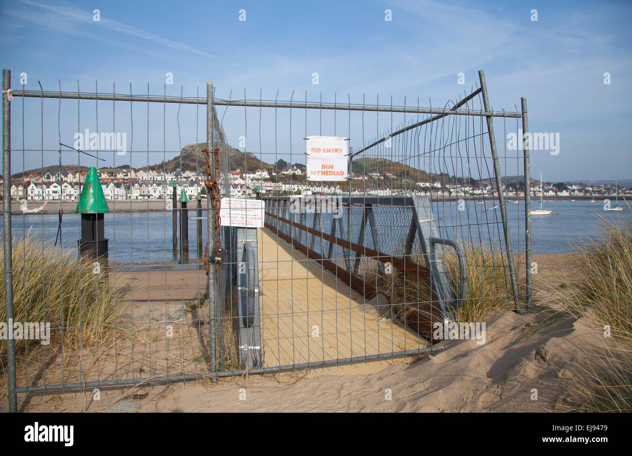 Wire mesh fencing and Warning Signs across a disused jetty at Conwy Harbour, North Wales at low tide and with Deganwy behind Stock Photo