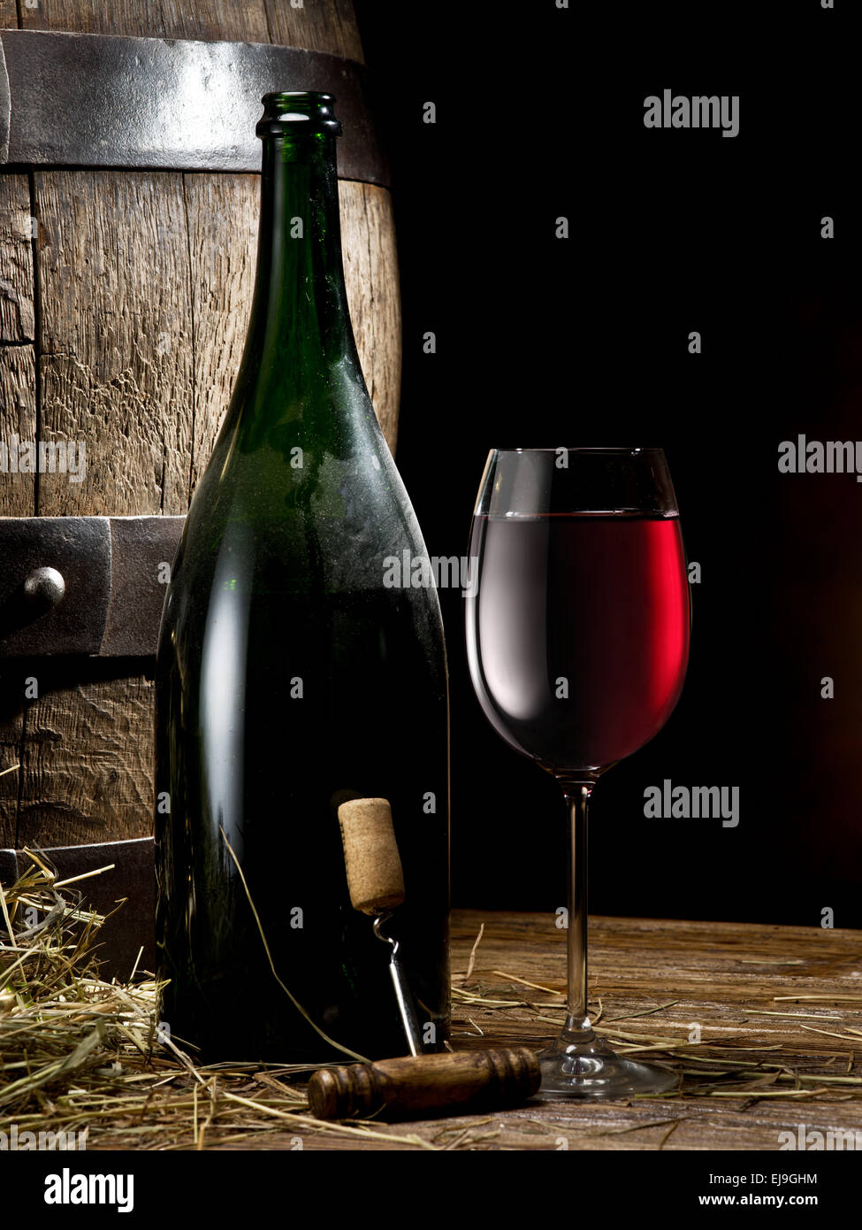 Still-life with glass of wine, bottle and barrel on the table in the cellar. Stock Photo