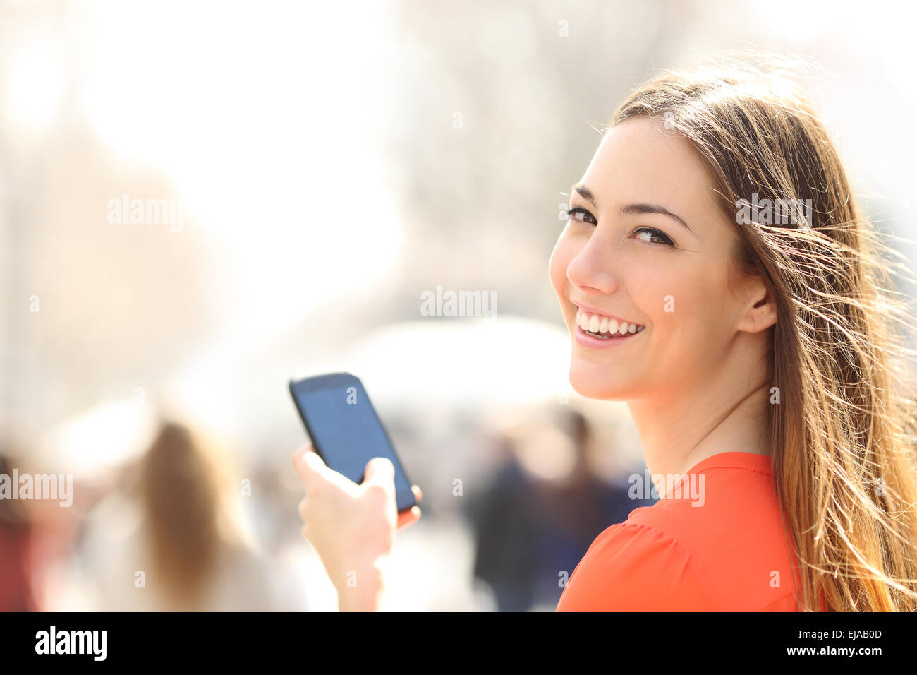 Happy woman smiling and walking in the street using a smartphone and looking at camera Stock Photo
