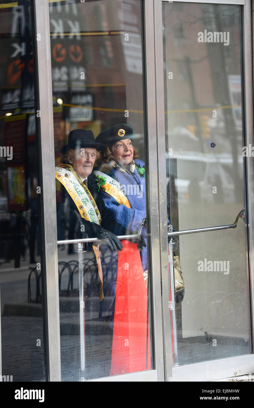 Two older persons look through a glass door the 2013 St. Patricks Day parade in Newark, New Jersey. USA. Stock Photo