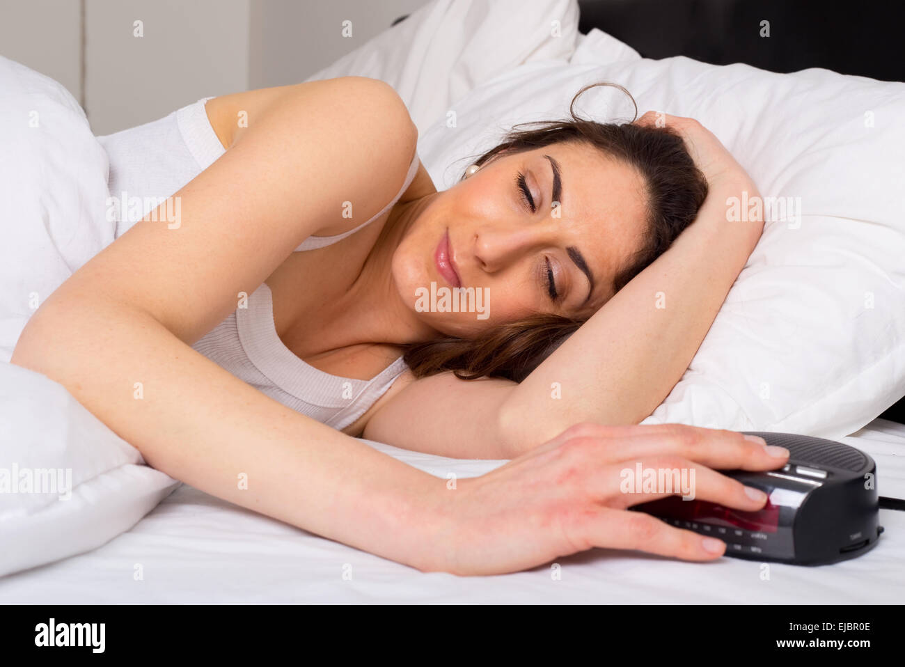 sleepy young woman switching off the alarm clock. Stock Photo