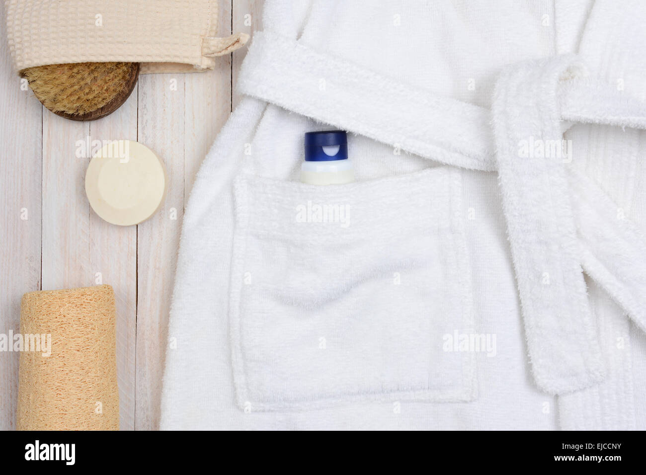 Closeup of a bathrobe with lotion in the pocket. A scrub brush and soap and a luffa are next to the robe on a rustic wooden surf Stock Photo