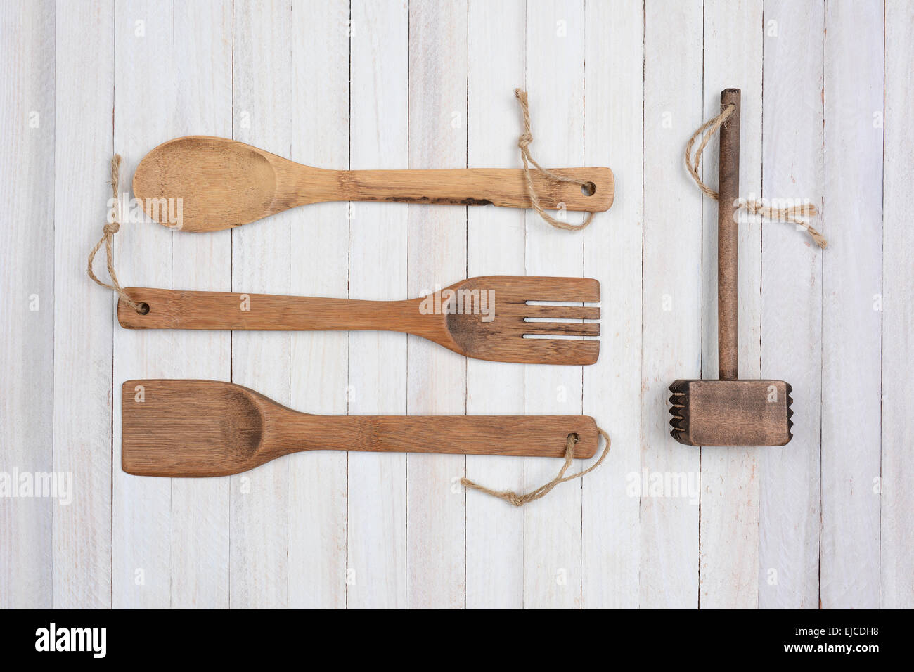 Overhead shot of four wooden kitchen utensils on a rustic white wood table. Items are: spoon, fork, spatula, and a mallet. Stock Photo